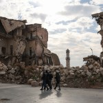 Syrians walk past one of Aleppo's destroyed structures near the northern city's historic citadel.